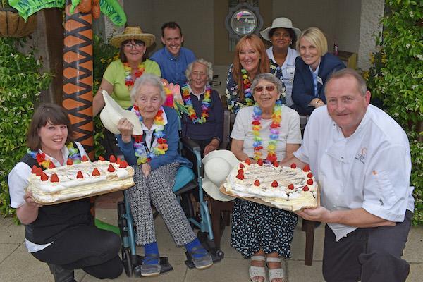 Caribbean twist: Residents Mary Bates, Jean Denham and Janette Banks enjoy the summer barbecue at Colten Care’s Belmore Lodge, including giant pavlovas, with staff including Home Manager Julie House (third right, back row).