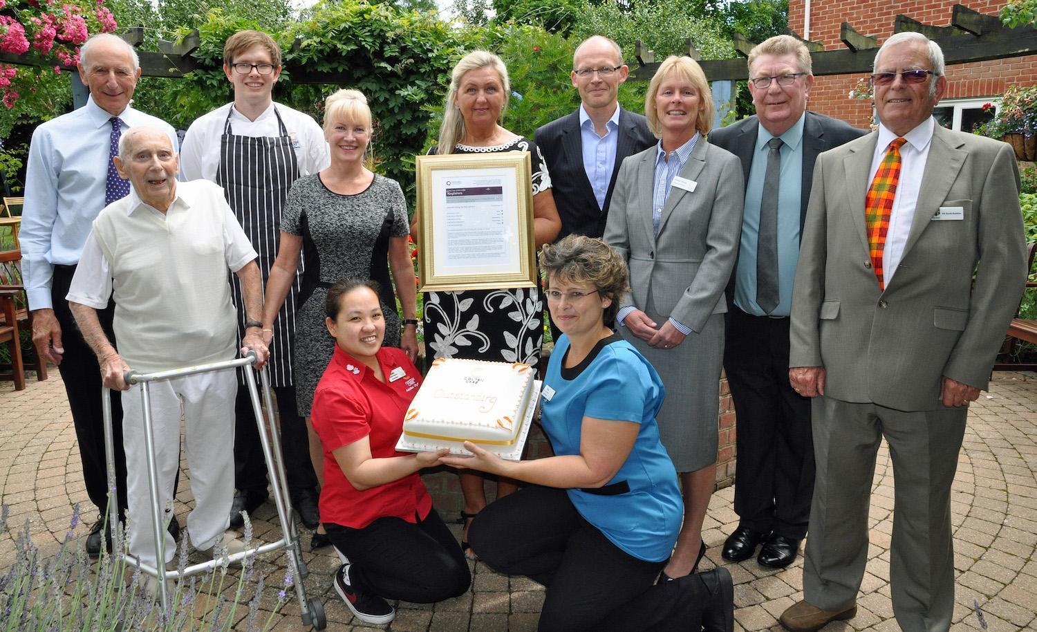 Beata Brzozowska, Home Manager (centre), with (left to right): John Colwell, joint founder of Colten Care; resident Eric Sinclare [CORRECT]; chef Rob Davies; Linda Brownlie, Operations Manager; Mark Aitchison, Chief Executive; Elaine Farrer., Operations Director; Tony Smith, Inspector, Care Quality Commission and Cllr David Hawkins, New Milton Town Council. Holding the cake are Rose Arcellana, Activity Organiser, and Kim Gritt, Care Coordinator.