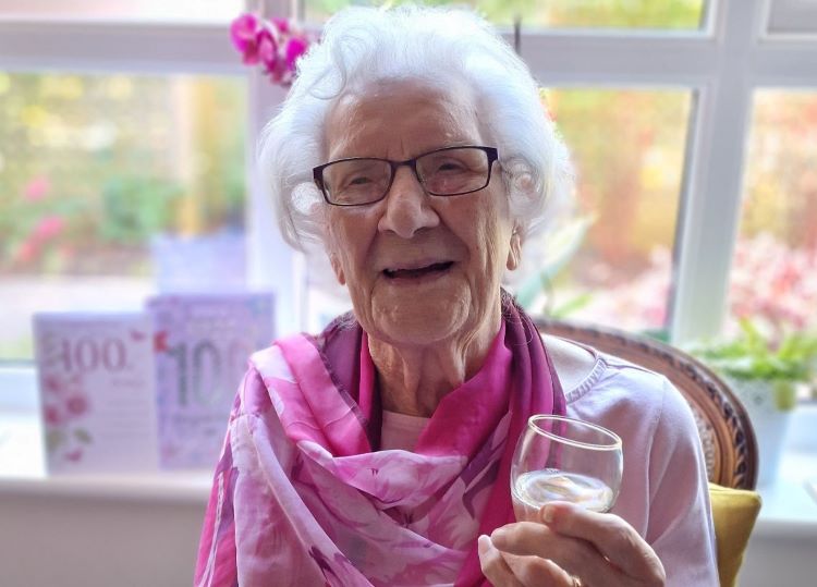 Centenarian Pat Dartnell dressed for her birthday party and holding a glass of wine
