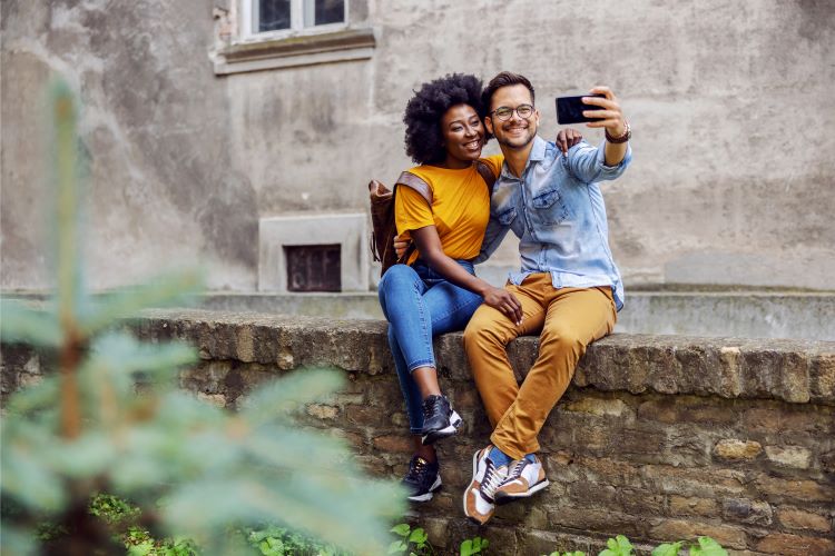 Couple taking selfie sitting on a wall outside a property