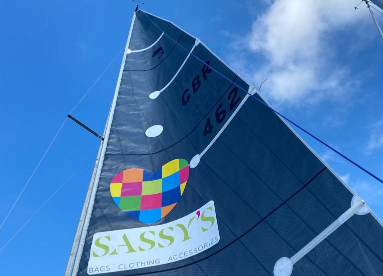 Yacht sail bearing Sassy's logo, with blue sky in background